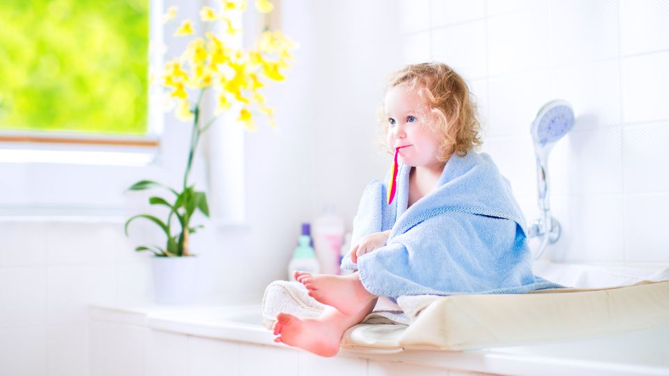 Little Girl Sitting In Bathroom With Brush In Her Mouth